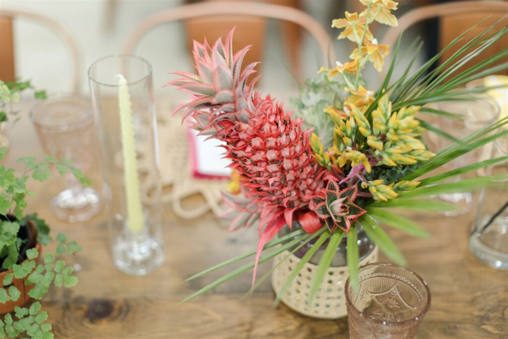 Close-up of vibrant tropical floral arrangement featuring orchids, greenery, and pink mini pineapples by Sarandipity Florals at Blooming Freedom venue
