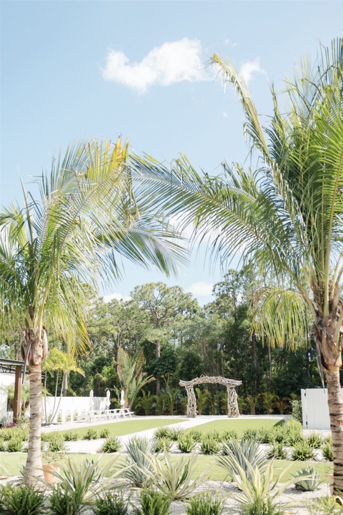 Blooming Freedom Palm City wedding ceremony space with driftwood style arch and paved center aisle bordered by low grass seating area